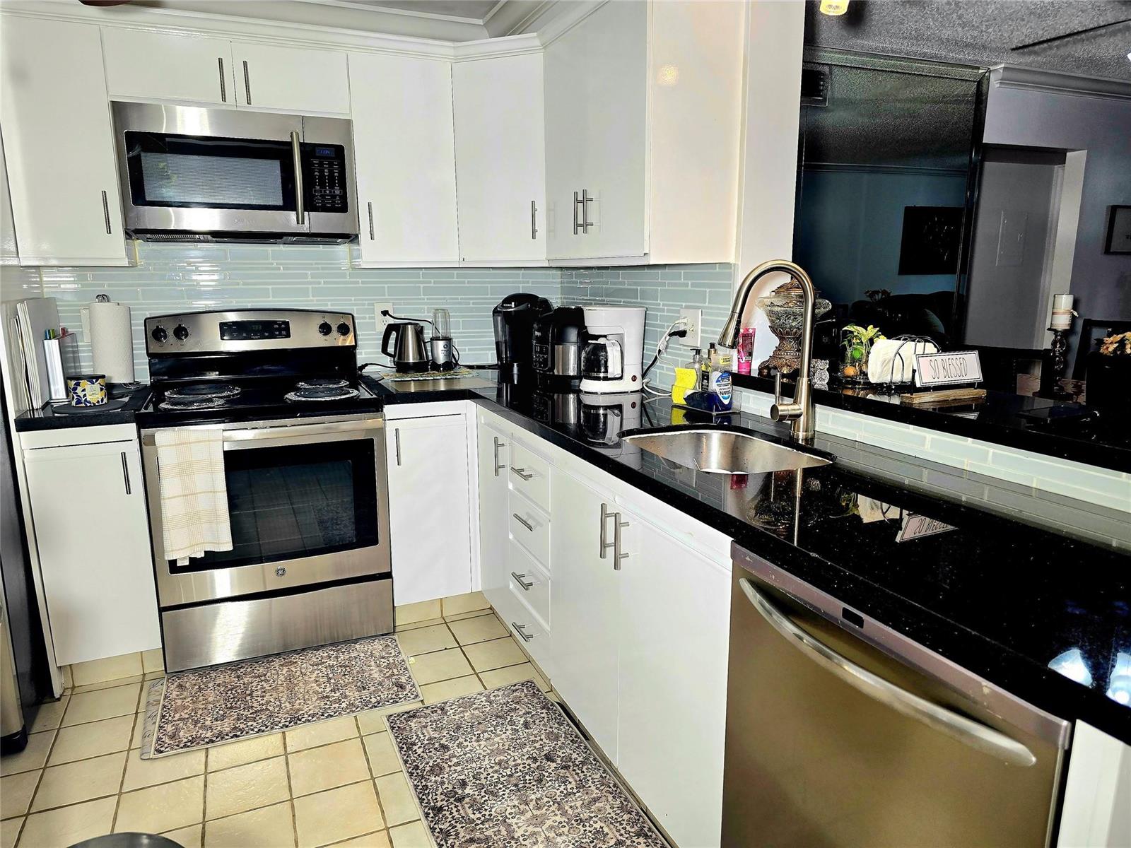 A kitchen features white cabinets, black countertops, stainless steel appliances, and a light blue backsplash — 2002 Granada Drive # K3, Coconut Creek FL 33066, COCONUT CREEK, FL