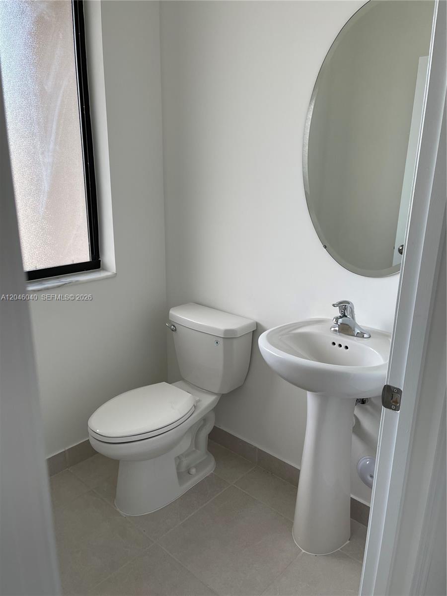 A small bathroom features a white pedestal sink, a toilet, and a round wall mirror — 21447 NE 2nd Pl, Miami FL 33179, MIAMI, FL