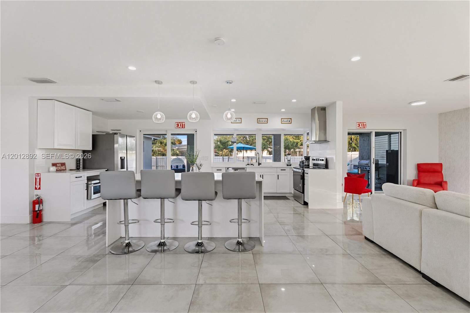 A modern open-concept kitchen features a central island with four bar stools and tile flooring — 632 S Crescent Dr, Hollywood FL 33021, HOLLYWOOD, FL