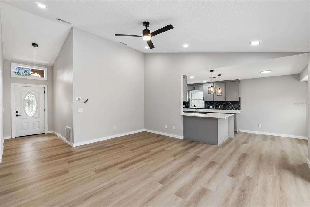 An open-concept living area features light wood-look flooring, a vaulted ceiling, and an adjacent kitchen — 761 ROBINHOOD DRIVE, MAITLAND, FL