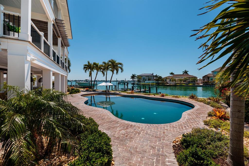 A swimming pool sits on a brick patio next to a house overlooking a canal — 5408 PALI WAY, ST PETE BEACH, FL