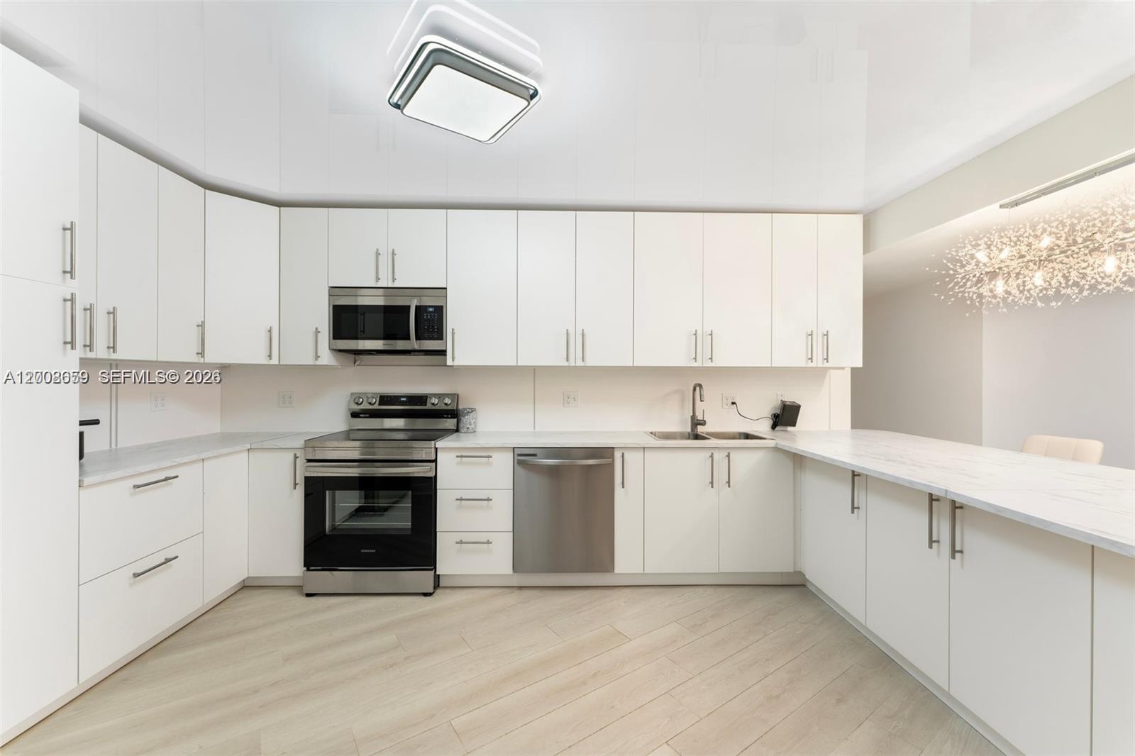 A modern kitchen features white cabinetry, stainless steel appliances, and light-colored wood-look flooring — 2500 Parkview Dr # 1714, Hallandale Beach FL 33009, HALLANDALE BEACH, FL