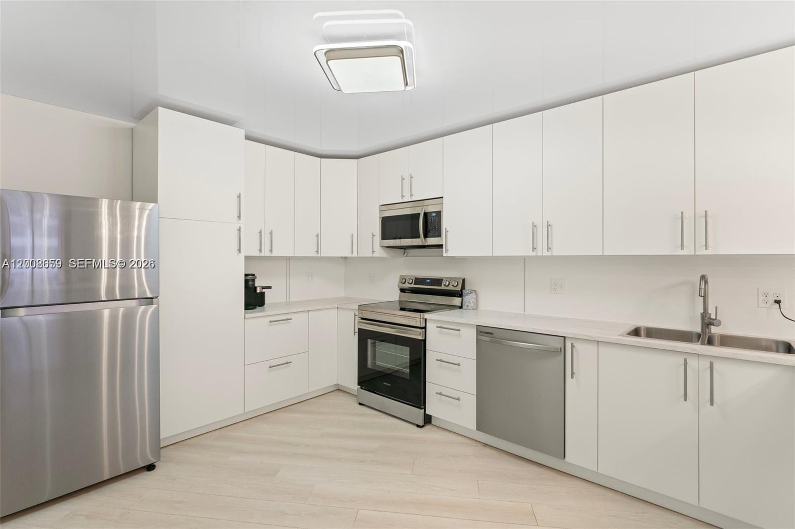 A modern kitchen features white cabinets, stainless steel appliances, and light wood-look flooring — 2500 Parkview Dr # 1714, Hallandale Beach FL 33009, HALLANDALE BEACH, FL