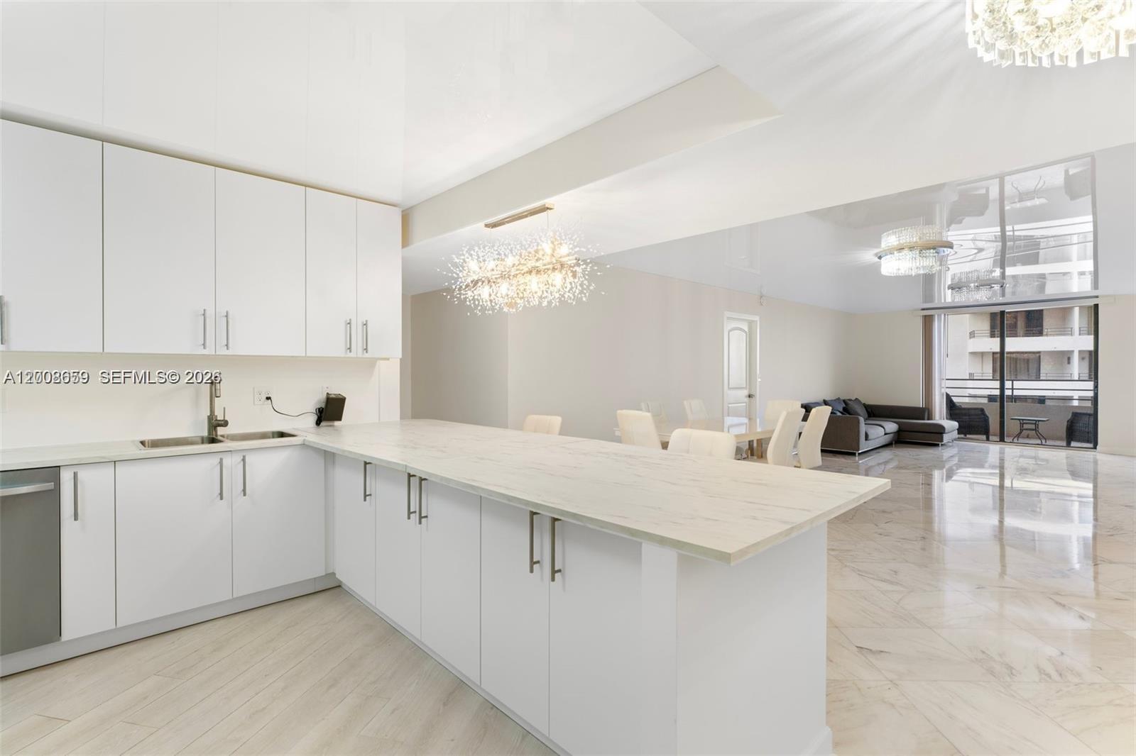 A modern kitchen with white cabinets and a marble countertop overlooks an open living area — 2500 Parkview Dr # 1714, Hallandale Beach FL 33009, HALLANDALE BEACH, FL