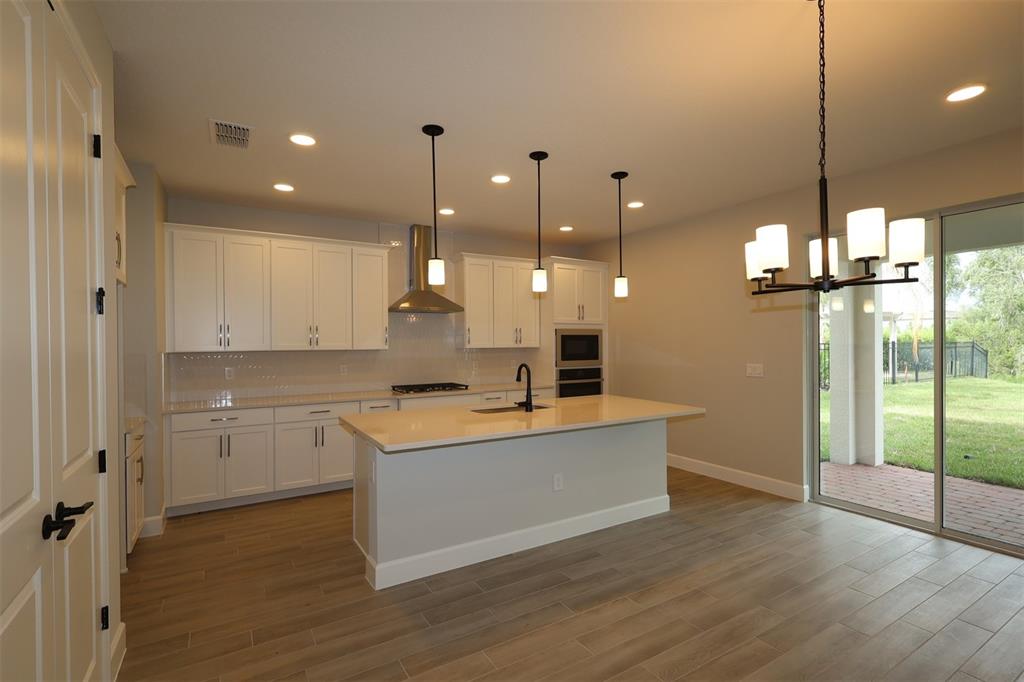 A modern kitchen and dining area with white cabinetry, a center island, and neutral furniture — 12033 ENCORE AT OVATION WAY, WINTER GARDEN, FL