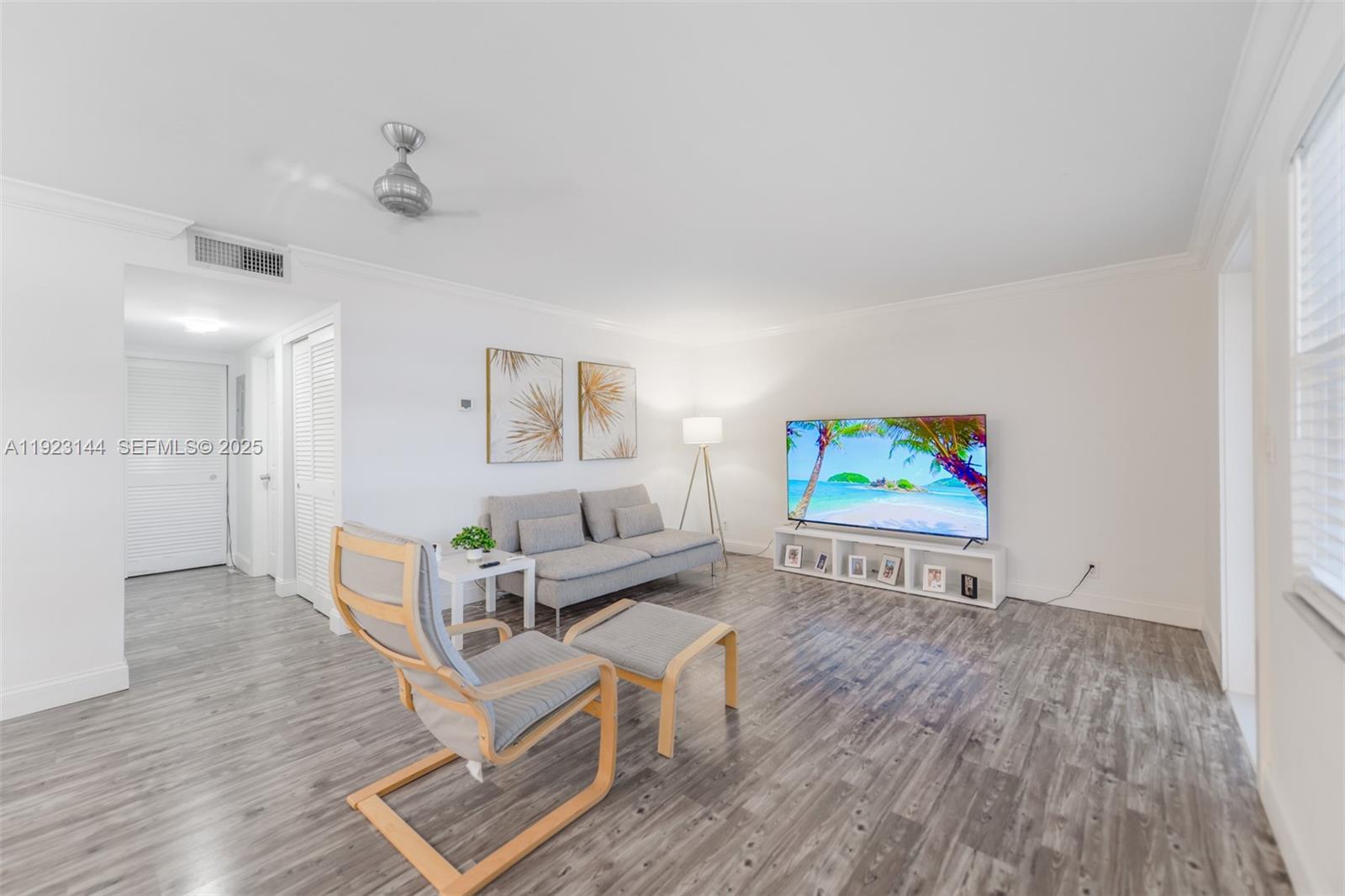 A living room features gray wood-look flooring, a sofa, an armchair with ottoman, and television — 200 NE 12th Ave # 6D, Hallandale Beach FL 33009, HALLANDALE BEACH, FL