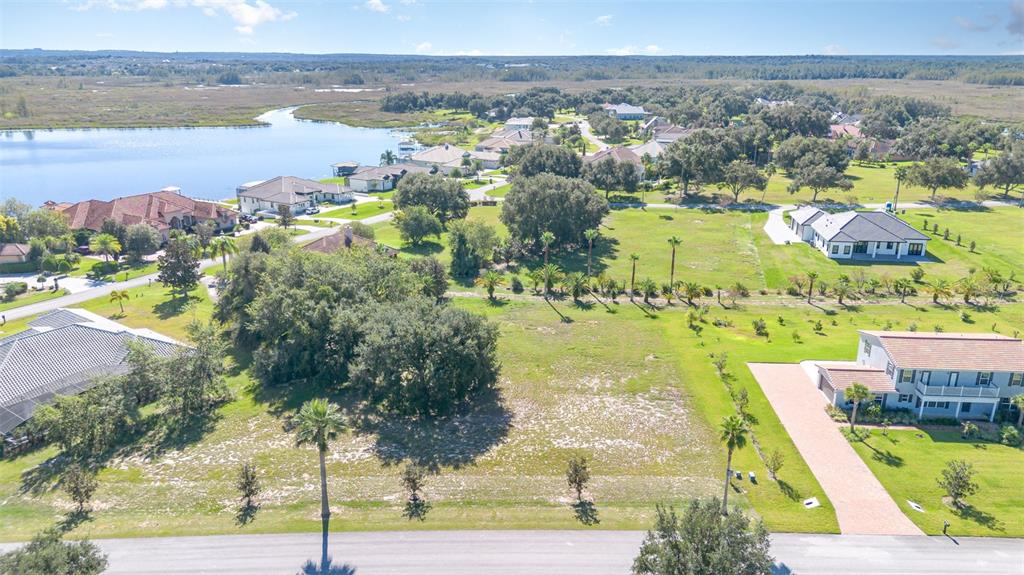 An aerial view shows a vacant residential lot surrounded by houses, trees, and a lake — 7434 JASMINE STREET, GROVELAND, FL