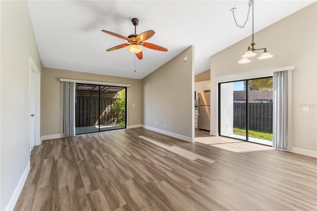 An open living and dining area with wood-look flooring, vaulted ceilings, and two sliding doors — 5201 BELLEFIELD DRIVE, TAMPA, FL