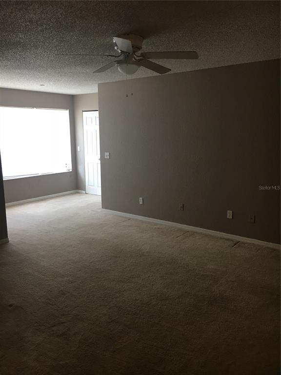 A carpeted living room features a ceiling fan, a large window, and a white door — 5112 CONROY ROAD UNIT 315, ORLANDO, FL
