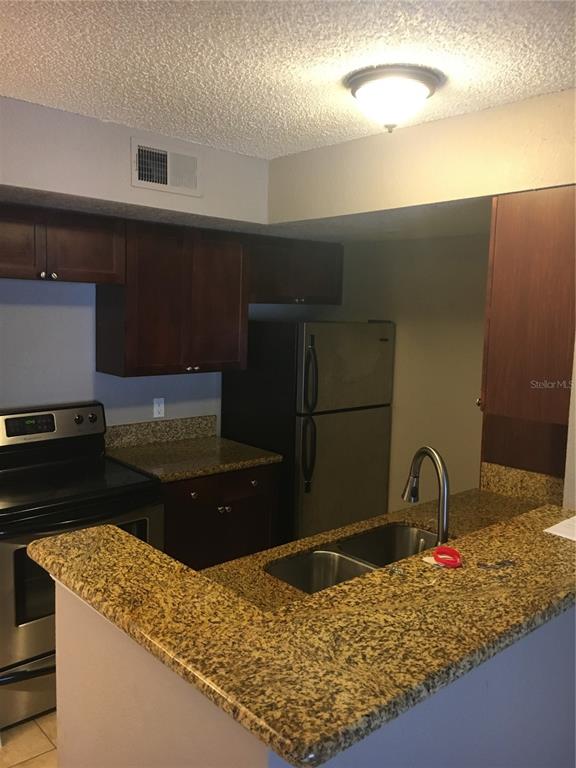 A kitchen features dark wood cabinets, granite countertops, stainless steel appliances, and a double sink — 5112 CONROY ROAD UNIT 315, ORLANDO, FL