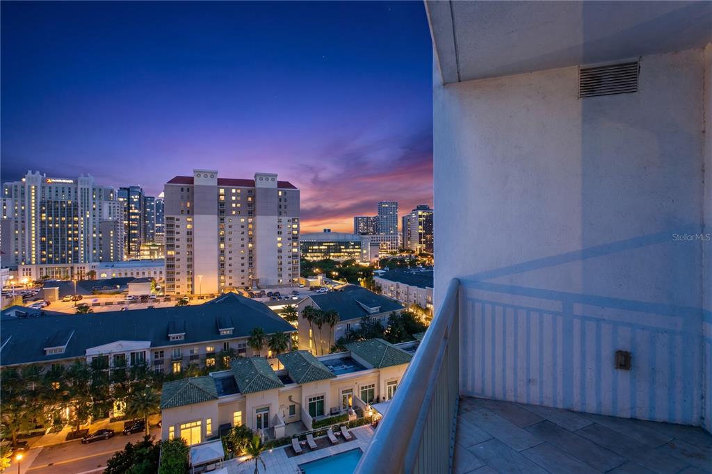 A balcony overlooks a city skyline at sunset with residential buildings and a pool below — 450 KNIGHTS RUN AVENUE UNIT 1208, TAMPA, FL