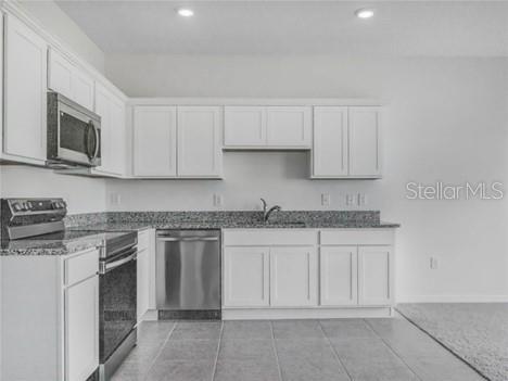 A kitchen features white cabinets, stainless steel appliances, and granite countertops over tiled flooring — 130 MANDOVI ST, DAVENPORT, FL
