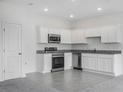 A kitchen with white cabinets and granite countertops transitions into a carpeted living area — 130 MANDOVI ST, DAVENPORT, FL