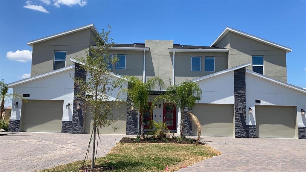 A two-story duplex with tan stucco, stone accents, two garages, and red front doors — 1149 DROP LANE UNIT 704, DAVENPORT, FL