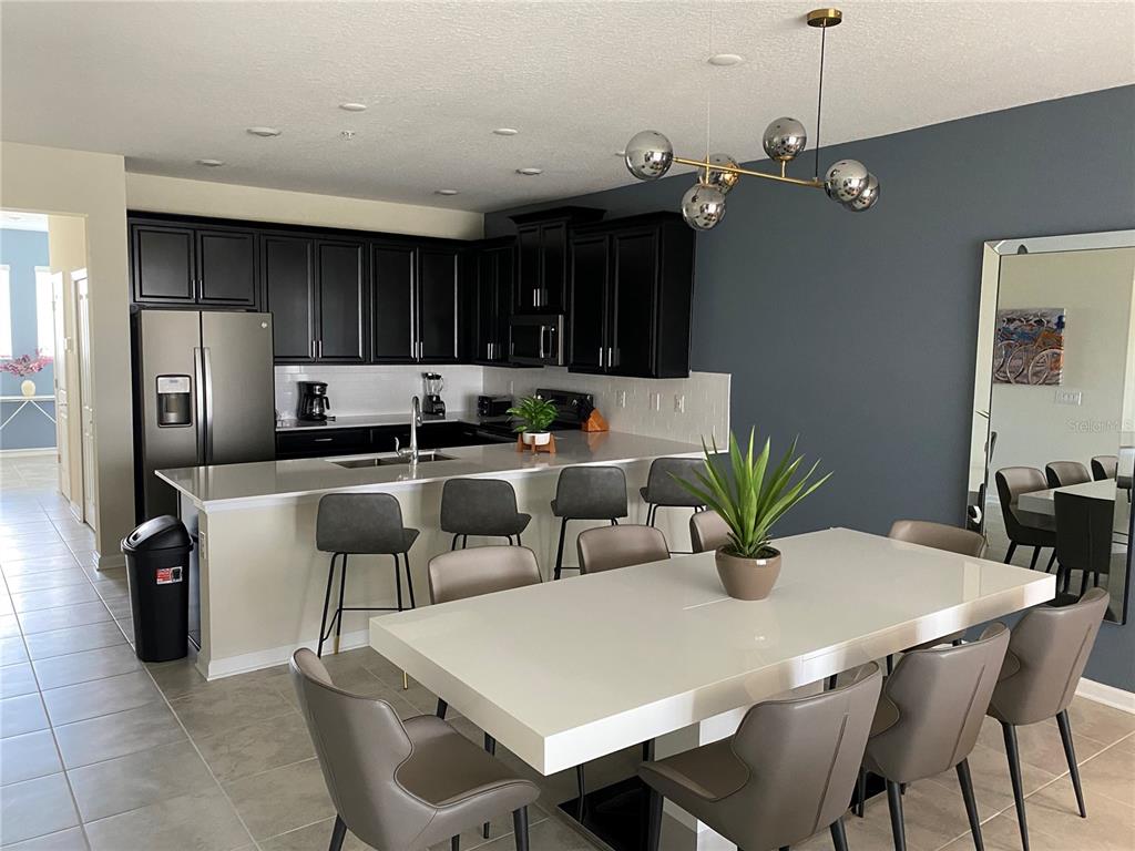 A modern kitchen with black cabinets and a dining area featuring a white table — 1149 DROP LANE UNIT 704, DAVENPORT, FL