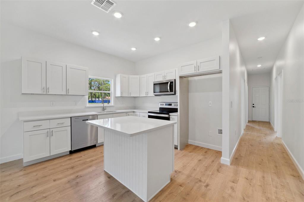 A modern kitchen features white cabinetry, stainless steel appliances, a center island, and wood-look flooring — 1724 ELIZABETH AVENUE, TITUSVILLE, FL