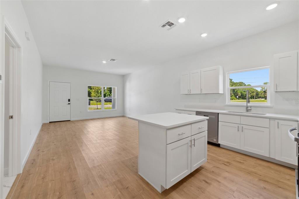 A bright, open-concept kitchen and living area featuring white cabinetry, an island, and wood flooring — 1724 ELIZABETH AVENUE, TITUSVILLE, FL