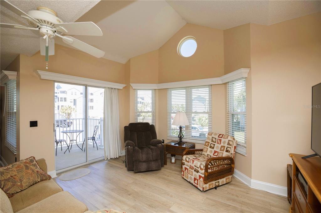 A living room features vaulted ceilings, light wood flooring, a ceiling fan, and a balcony — 5712 BISCAYNE COURT UNIT 101, NEW PORT RICHEY, FL
