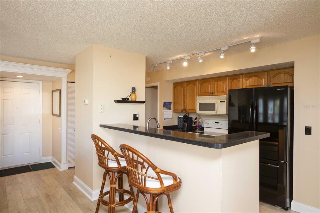 A kitchen features a breakfast bar, wooden cabinets, black appliances, and light-colored wood flooring — 5712 BISCAYNE COURT UNIT 101, NEW PORT RICHEY, FL