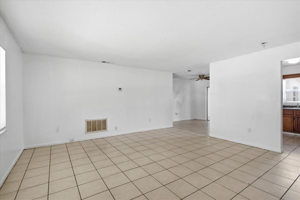 An empty room with white walls, beige tile flooring, and a view into a kitchen — 4817 BLARNEY DRIVE, ORLANDO, FL