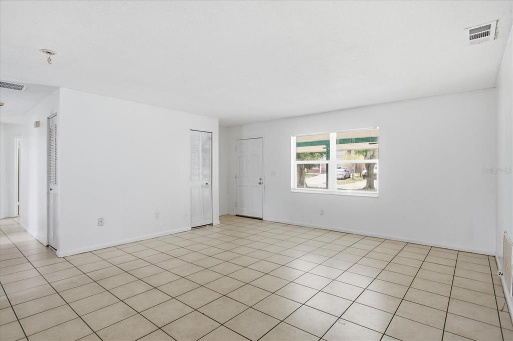 An empty living room with white walls, beige tile flooring, and a single window — 4817 BLARNEY DRIVE, ORLANDO, FL