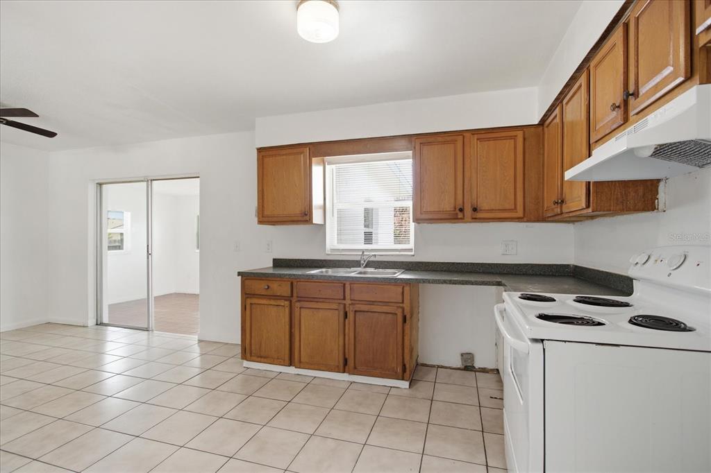 A kitchen features wood cabinets, a white stove, a sink, and light-colored floor tiles — 4817 BLARNEY DRIVE, ORLANDO, FL