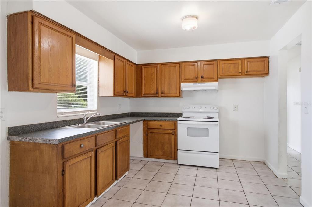 A kitchen with wood cabinets, a white stove, gray countertops, and light-colored tile flooring — 4817 BLARNEY DRIVE, ORLANDO, FL