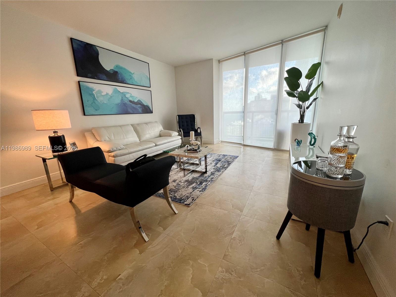 A modern living room features a white sofa, black chaise lounge, and large floor-to-ceiling windows — 495 Brickell Ave # 2707, Miami FL 33131, MIAMI, FL