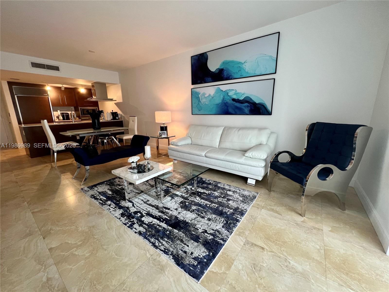 A modern living room features a white sofa, blue accent chair, and abstract wall art — 495 Brickell Ave # 2707, Miami FL 33131, MIAMI, FL