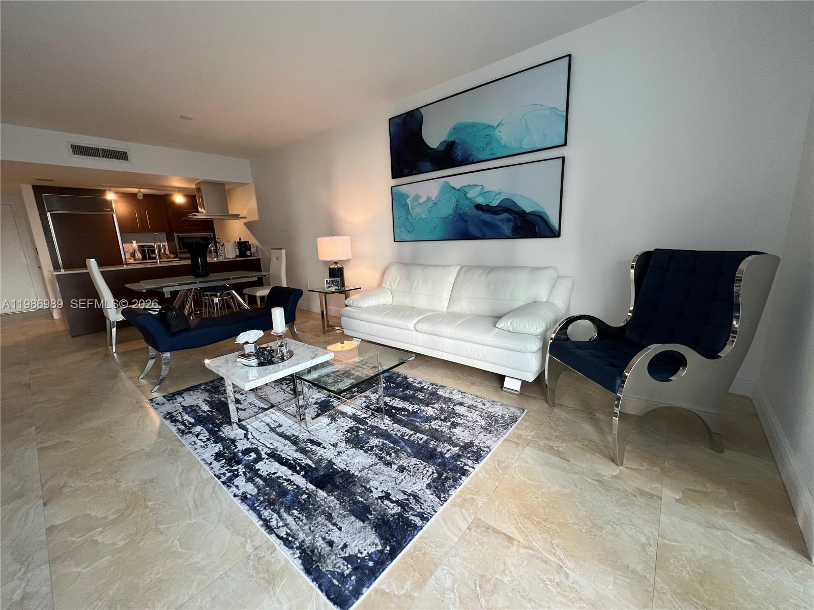 A living room features a white sofa, blue accent chairs, and a patterned area rug — 495 Brickell Ave # 2707, Miami FL 33131, MIAMI, FL