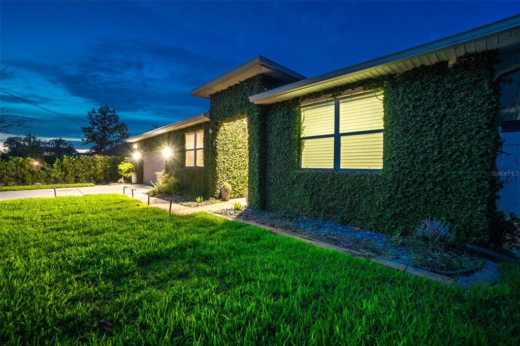 A single-story house exterior is covered in climbing ivy and illuminated at dusk — 59 BEAVERDAM LANE, PALM COAST, FL