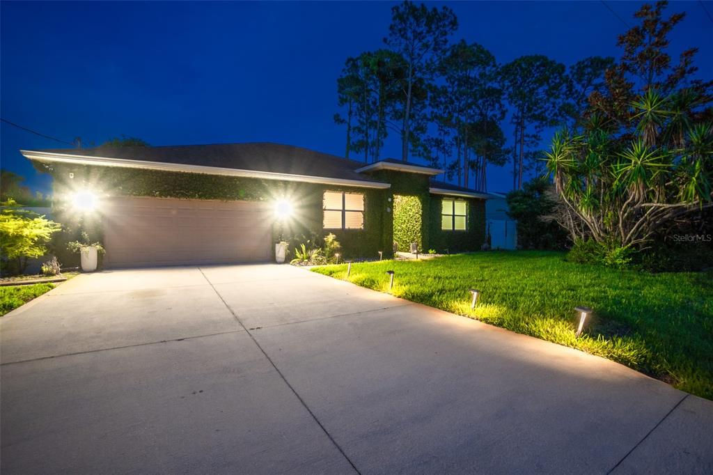A single-story house with a concrete driveway and ivy-covered exterior walls at dusk — 59 BEAVERDAM LANE, PALM COAST, FL