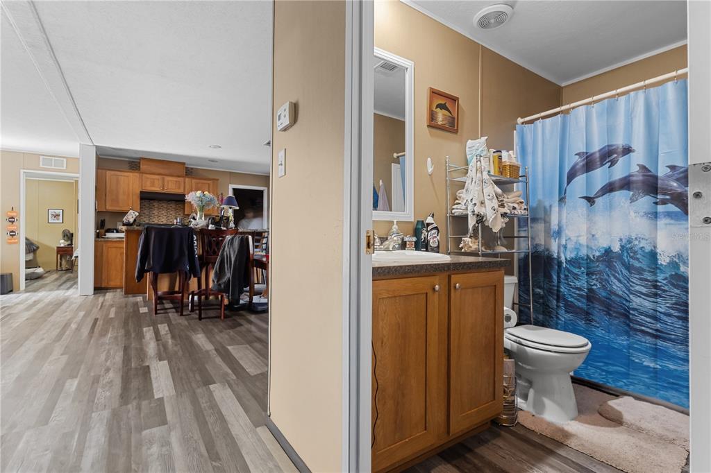 A bathroom with a wood vanity and dolphin shower curtain opens to a kitchen area — 1650 W LYMAN HENDRY ROAD UNIT 1, PERRY, FL