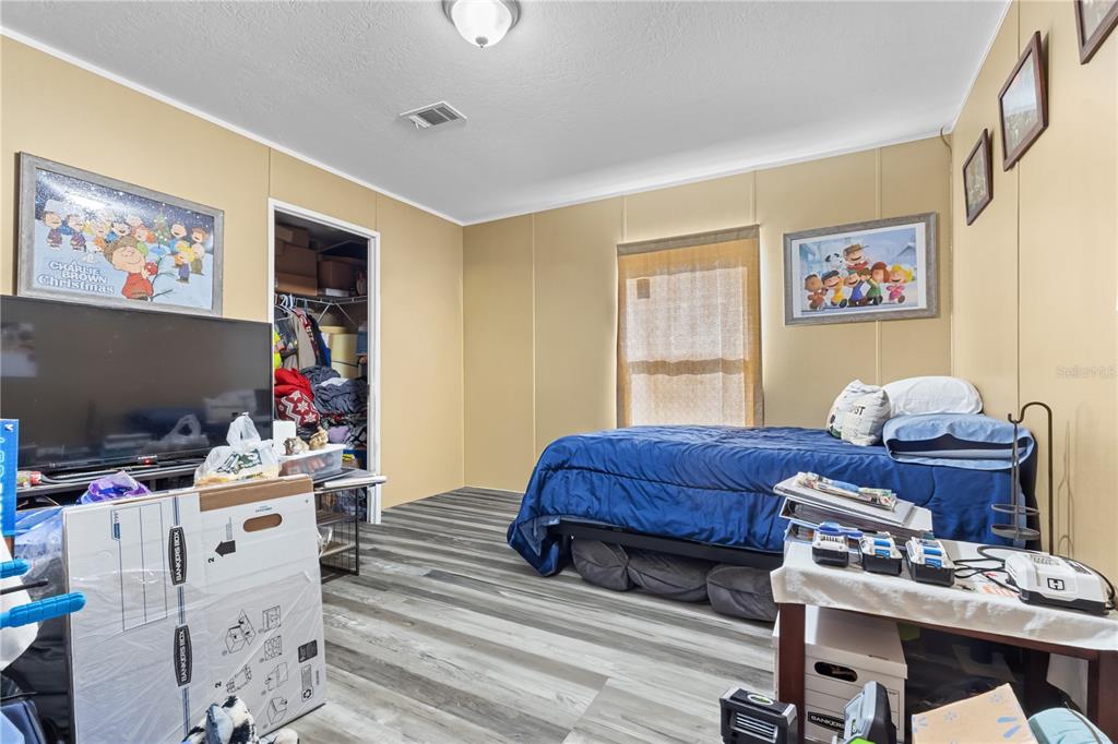 A bedroom features tan walls, wood-look flooring, a bed with blue bedding, and a closet — 1650 W LYMAN HENDRY ROAD UNIT 1, PERRY, FL