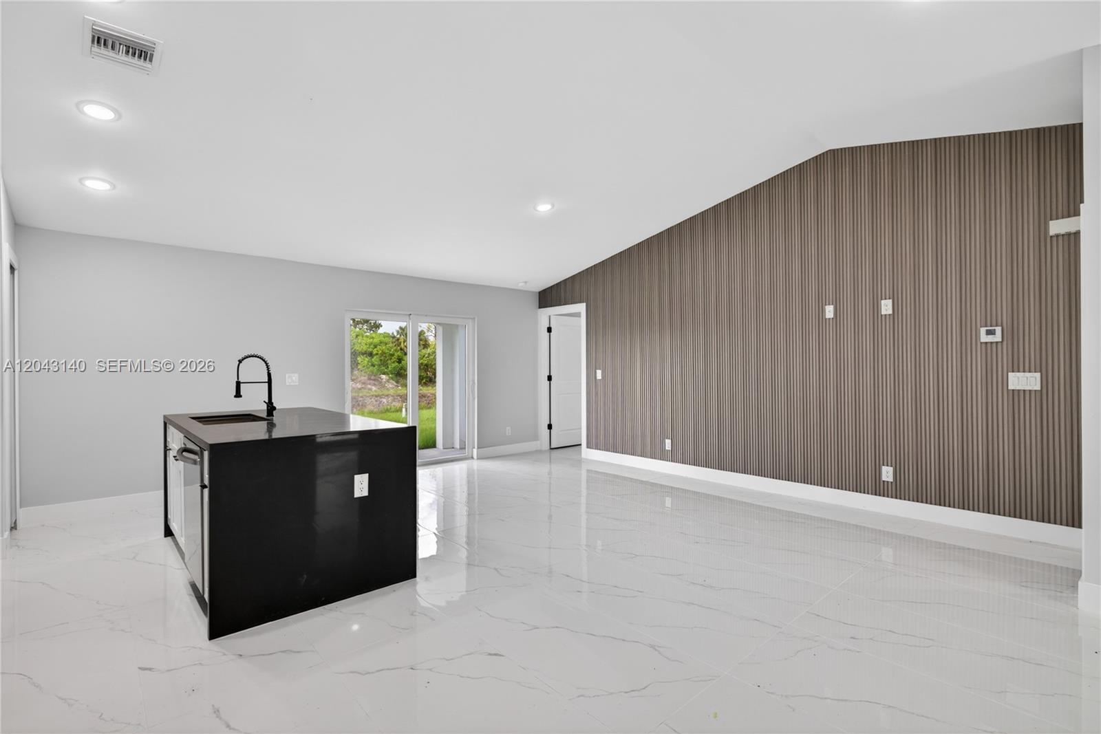 A modern kitchen and living area features a black island, white tile floors, and slatted walls — 704 E Carbon, Lehigh Acres FL 33974, LEHIGH ACRES, FL