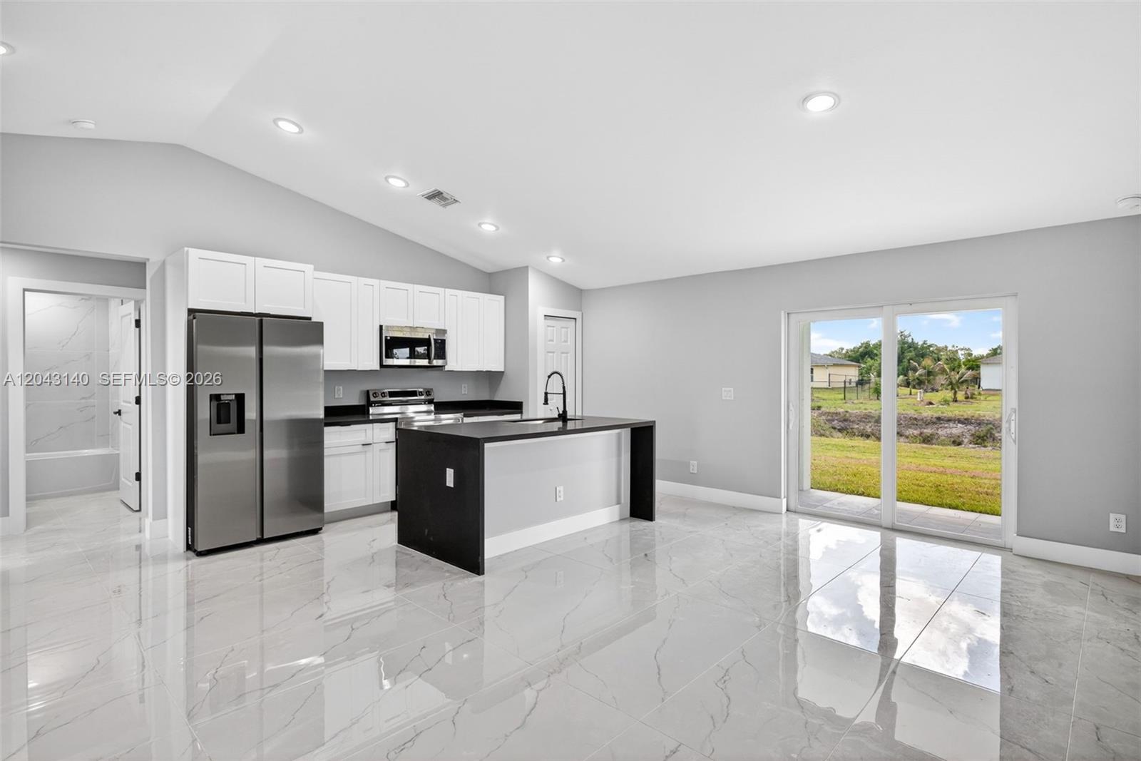 A modern kitchen features white cabinetry, a black island, stainless steel appliances, and tile flooring — 704 E Carbon, Lehigh Acres FL 33974, LEHIGH ACRES, FL