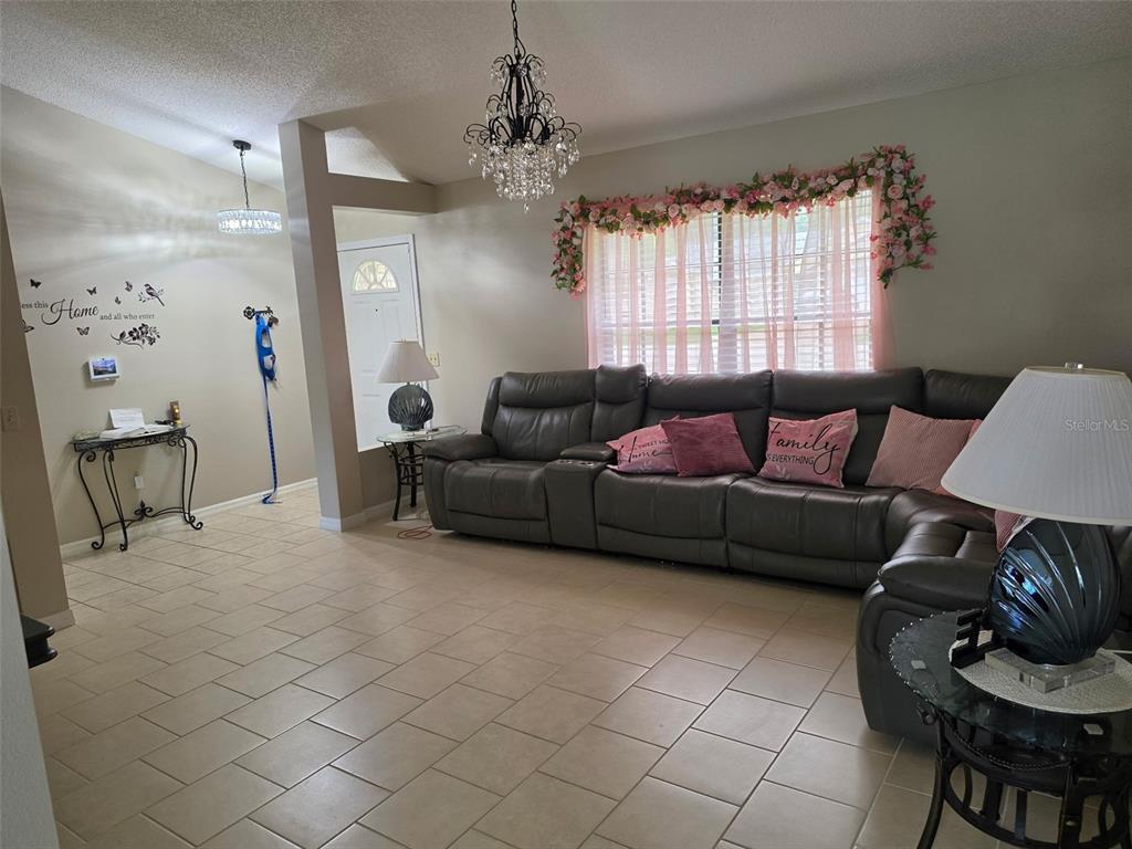 A living room features a large gray sectional sofa, tile flooring, and a crystal chandelier — 2824 SUNSET RIDGE ST, DELTONA, FL