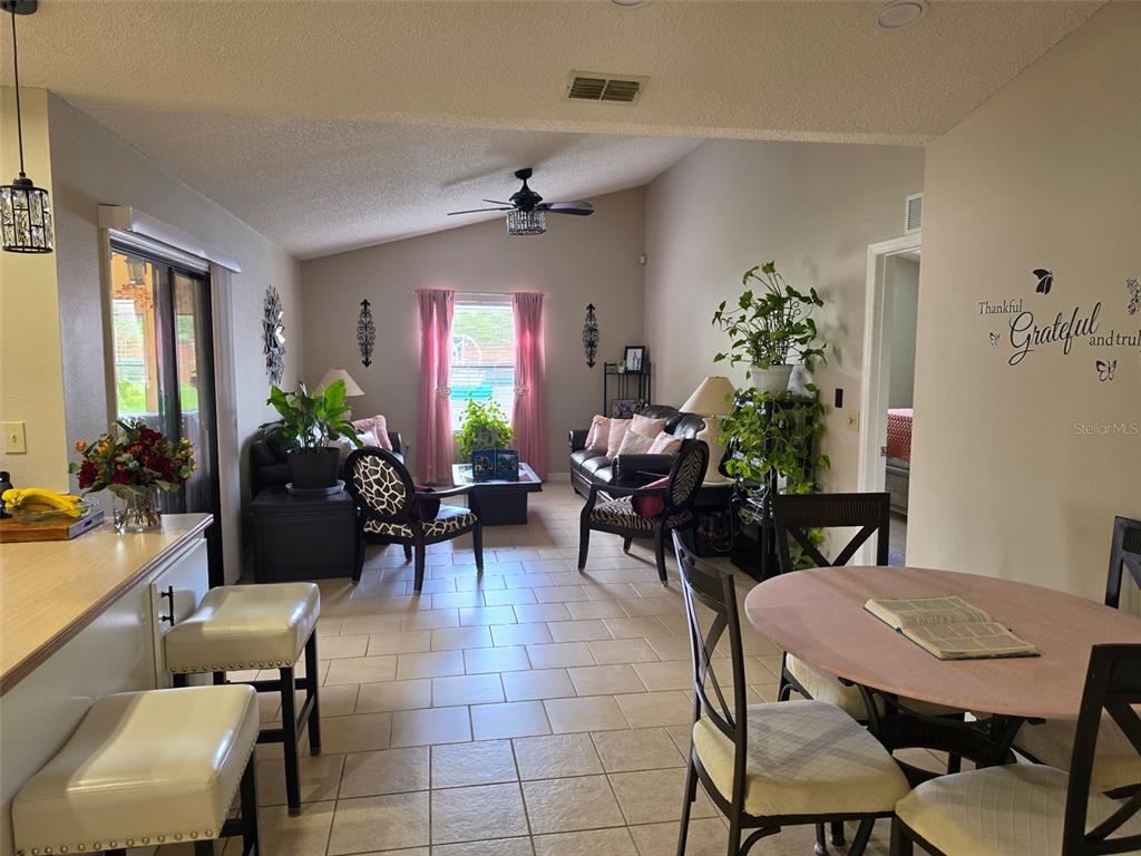 An open-concept living and dining area features tile flooring, vaulted ceilings, and a kitchen island — 2824 SUNSET RIDGE ST, DELTONA, FL