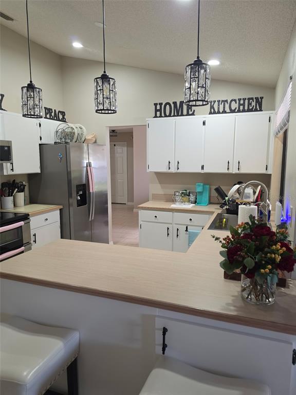 A kitchen features white cabinets, light wood countertops, stainless steel appliances, and three pendant lights — 2824 SUNSET RIDGE ST, DELTONA, FL