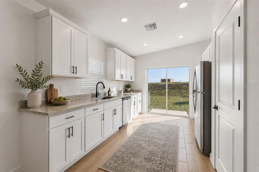 A kitchen with white cabinets, granite countertops, stainless steel appliances, and a sliding glass door — 561 BLACKTHORN DRIVE, LAKELAND, FL