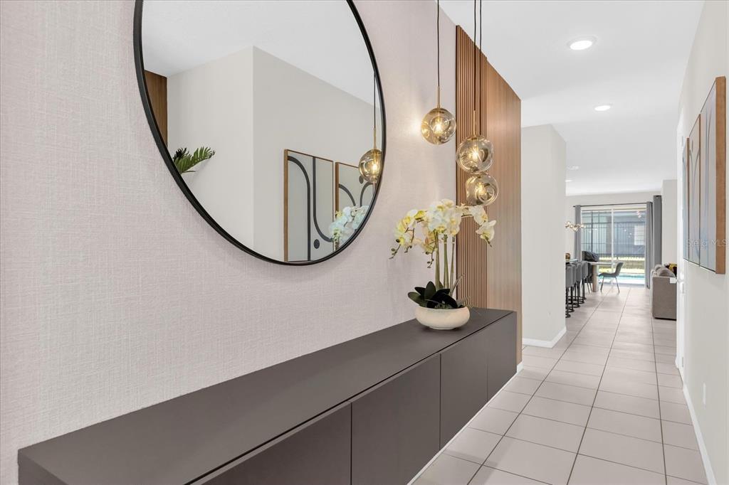 A modern entryway features a floating dark cabinet, a large round mirror, and pendant lighting — 9012 EGRET MILLS TERRACE, KISSIMMEE, FL