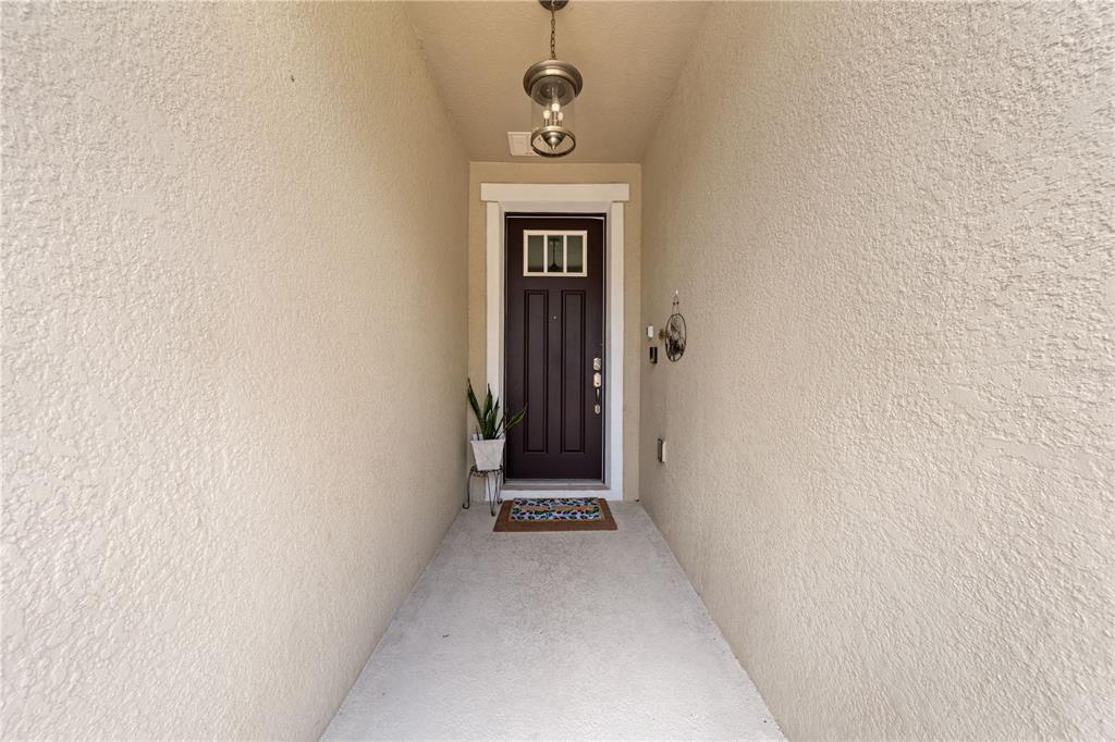 A covered entryway features a dark brown front door, a light fixture, and textured walls — 4704 RUBY RED LANE, KISSIMMEE, FL