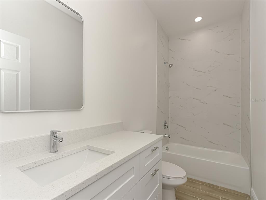 A bathroom features a white vanity, a rectangular mirror, and a tub-shower with marble-look tile — 1216 S POMEGRANITE AVENUE, SANFORD, FL