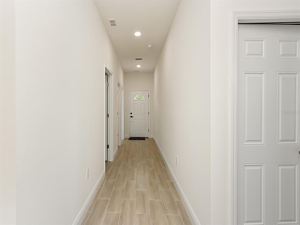 A hallway with light-colored tile flooring and white walls leads to a front door — 1216 S POMEGRANITE AVENUE, SANFORD, FL
