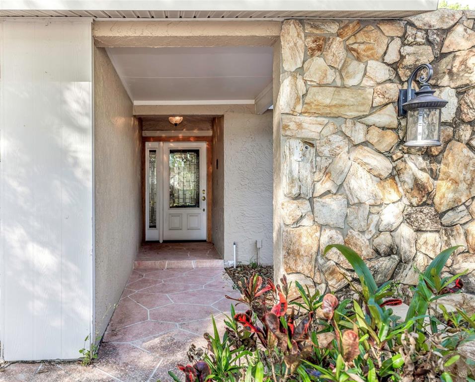 A covered entryway features a stone wall, a lantern light, and a glass-paneled front door — 4101 WINDTREE DRIVE, TAMPA, FL