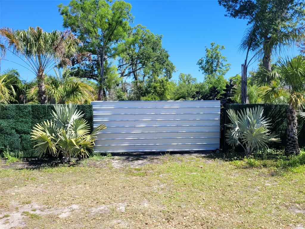 A white metal gate stands between two sections of green privacy fencing in a yard — 7513 EDGEWATER DRIVE, ORLANDO, FL