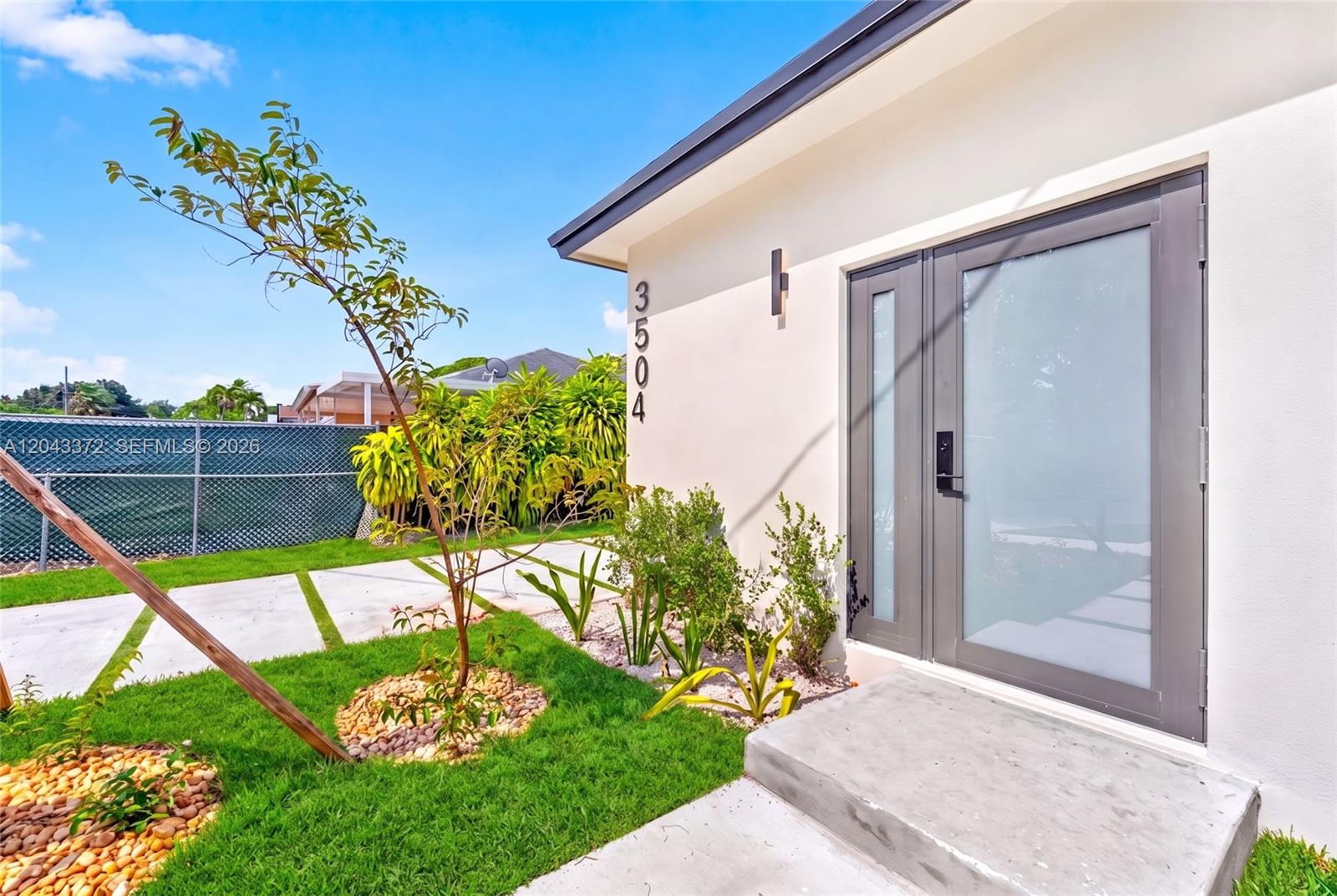A modern home exterior features a frosted glass front door and a concrete walkway — 3506 NW 9th Ave, Miami FL 33127, MIAMI, FL