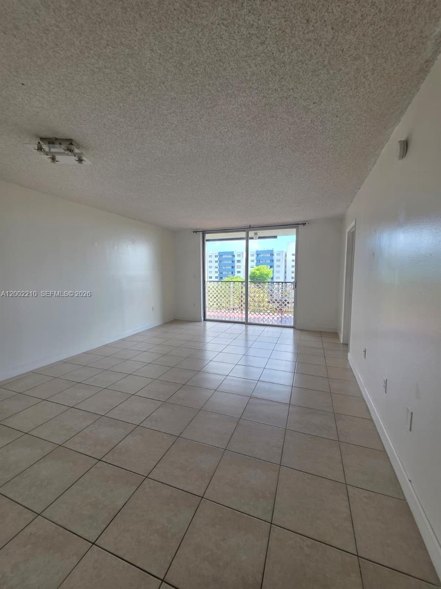 An empty living room features beige tile flooring, white walls, and a sliding glass balcony door — 5055 NW 7th St # 602, Miami FL 33126, MIAMI, FL