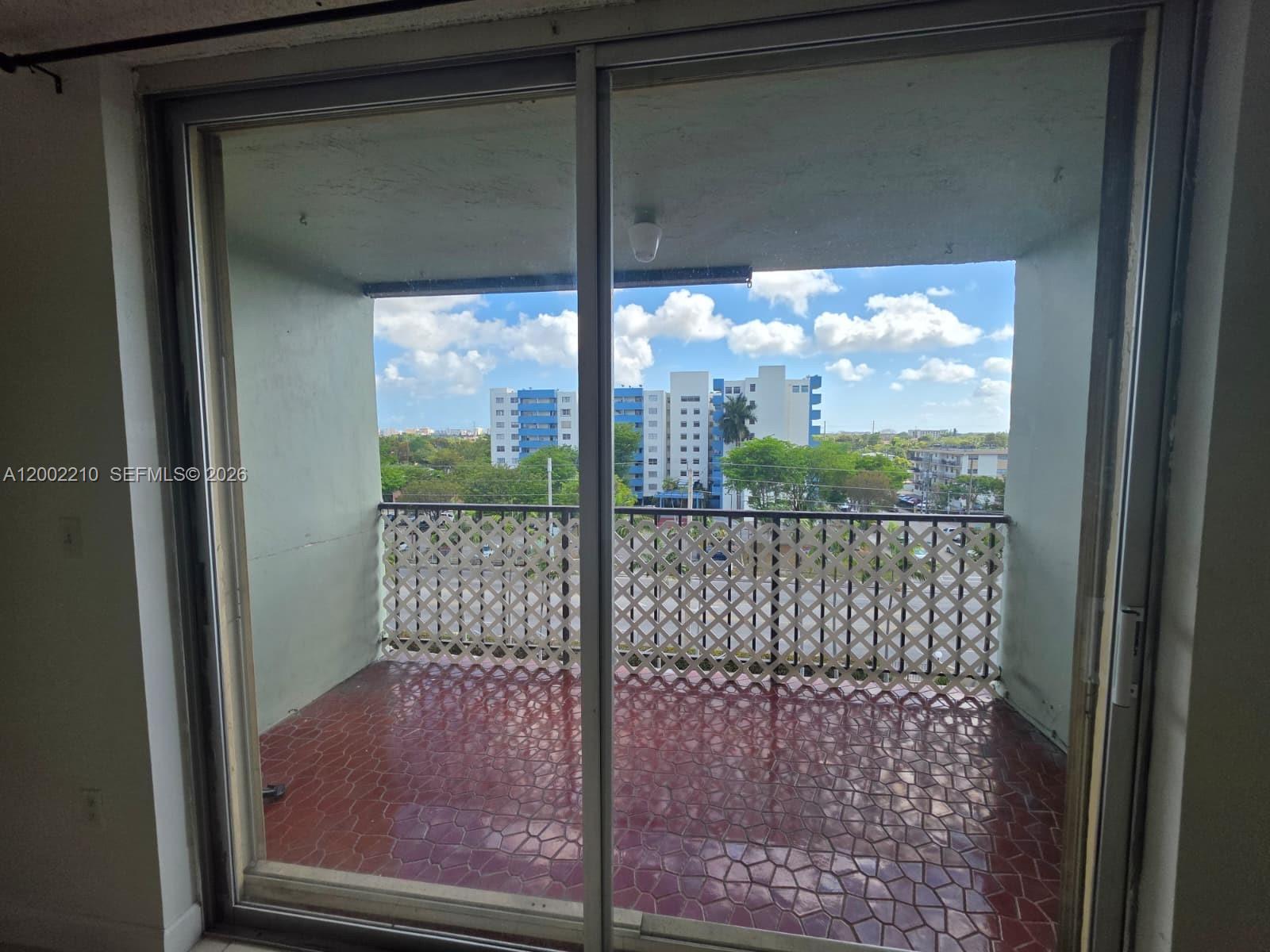 A balcony with red tiled flooring and a white lattice railing overlooks a city view — 5055 NW 7th St # 602, Miami FL 33126, MIAMI, FL