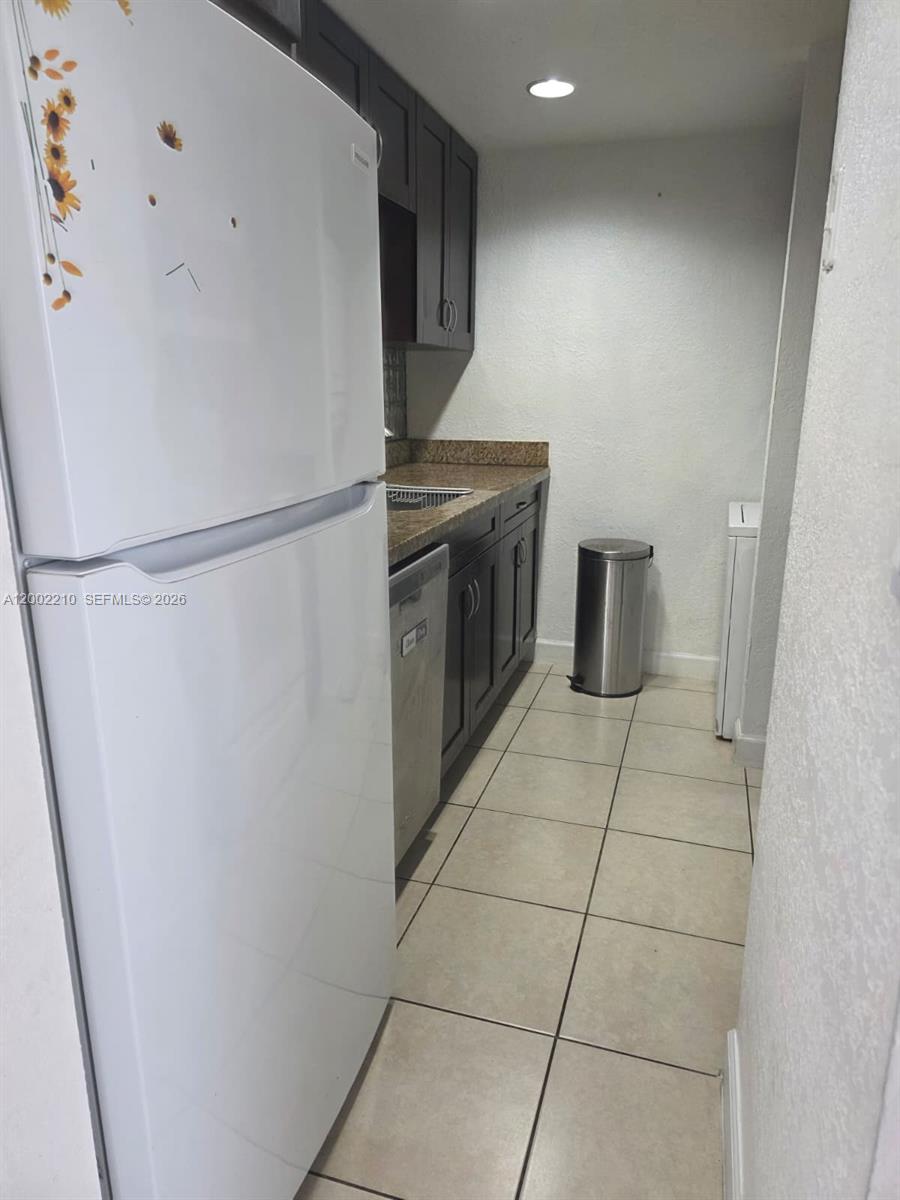 A galley kitchen features dark cabinets, granite countertops, a white refrigerator, and tiled flooring — 5055 NW 7th St # 602, Miami FL 33126, MIAMI, FL